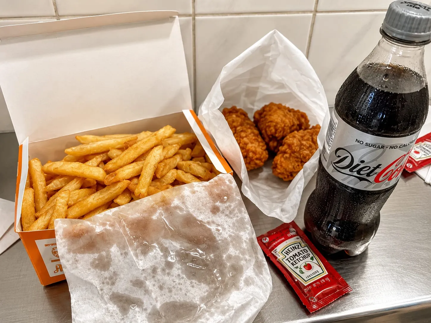 Chips, chicken pieces and a cold drink laid out on the counter